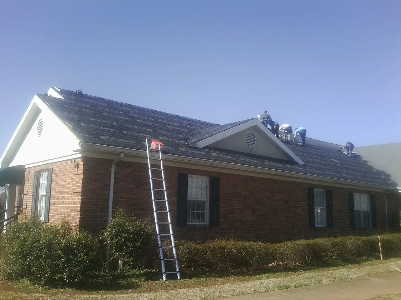 Crew tearing shingles off a brick ranch roof with a ladder set — Metal Roof Repair work by our crew in Camp Murray