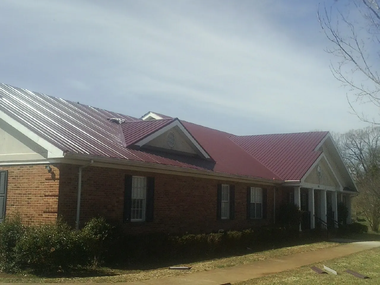 Red metal roof with gabled entries on a long brick building, from a Hail Damage Roof Repair job in Camp Murray