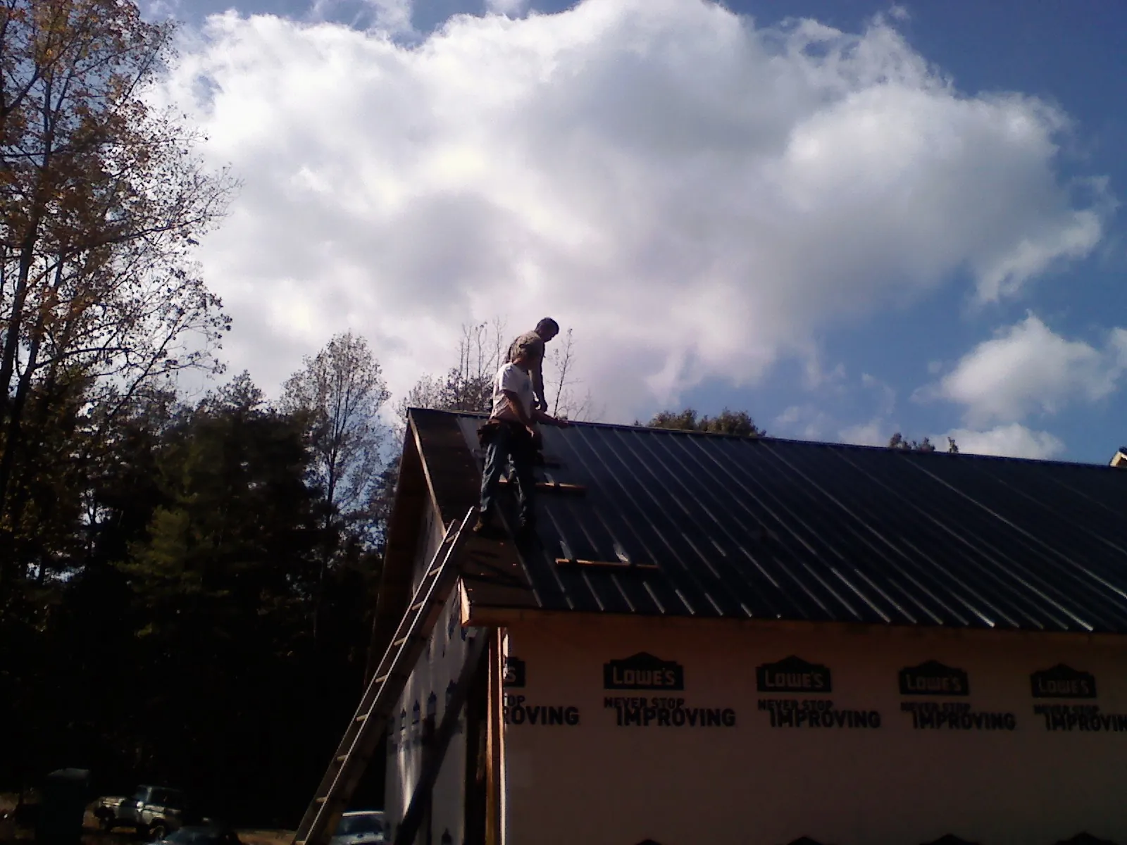 Roofer fastening dark metal panels high against a cloudy sky, from a Roof Inspection job in Camp Murray