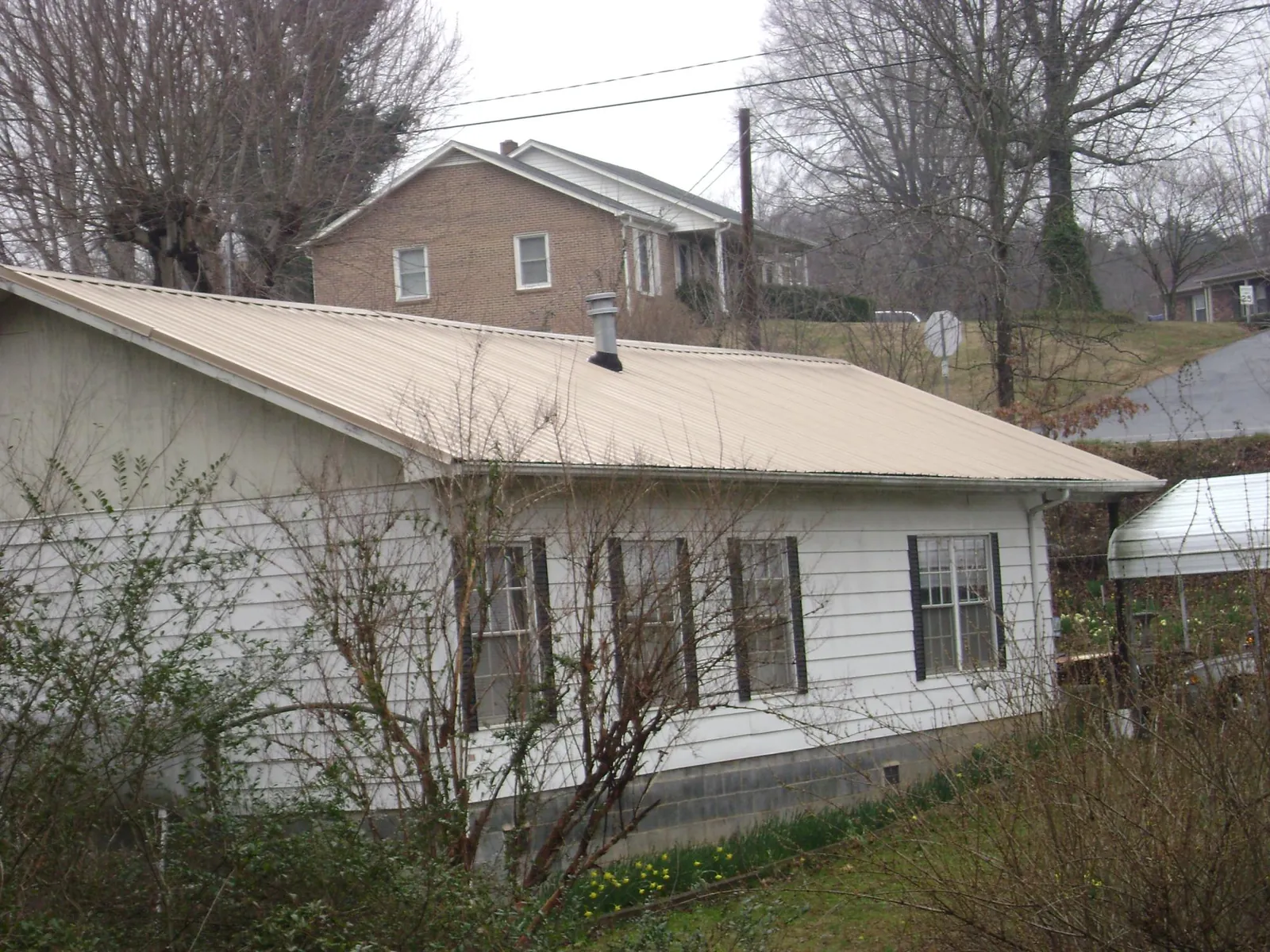 Tan metal roof on a white sided house set into a hillside — Commercial Roofing by Roofing Brothers in Camp Murray